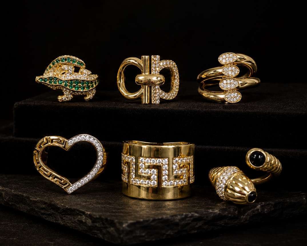 A collection of gold rings with various gemstone and crystal designs, displayed on a dark wooden surface and a black pedestal against a black background.
